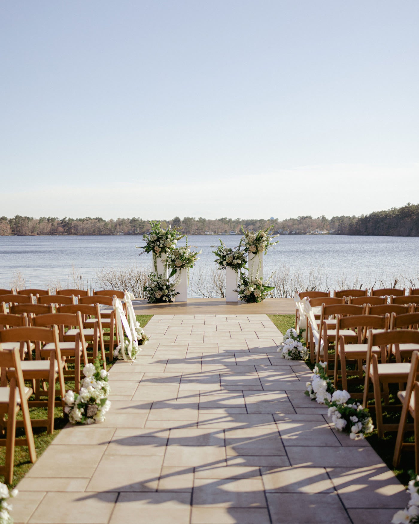 A lakeside ceremony aisle lined with chairs and white blooms
