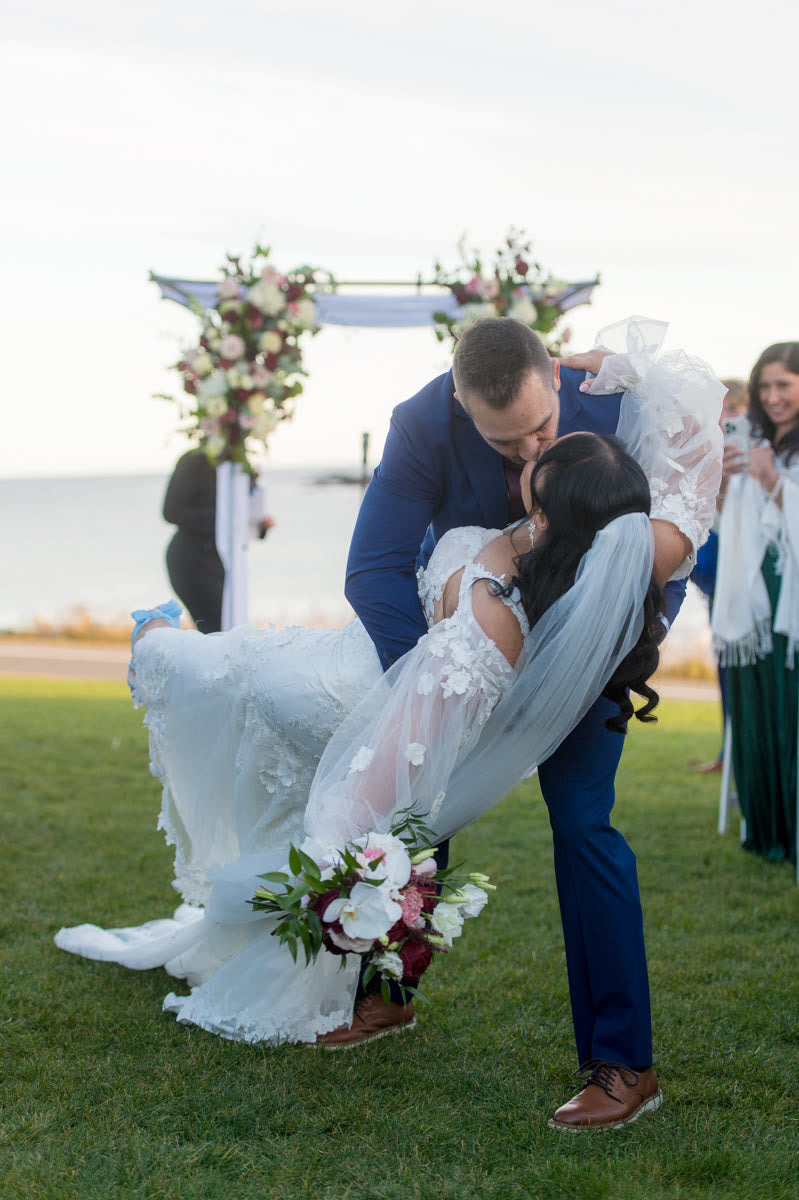 Groom dipping the bride beneath the oceanfront arch