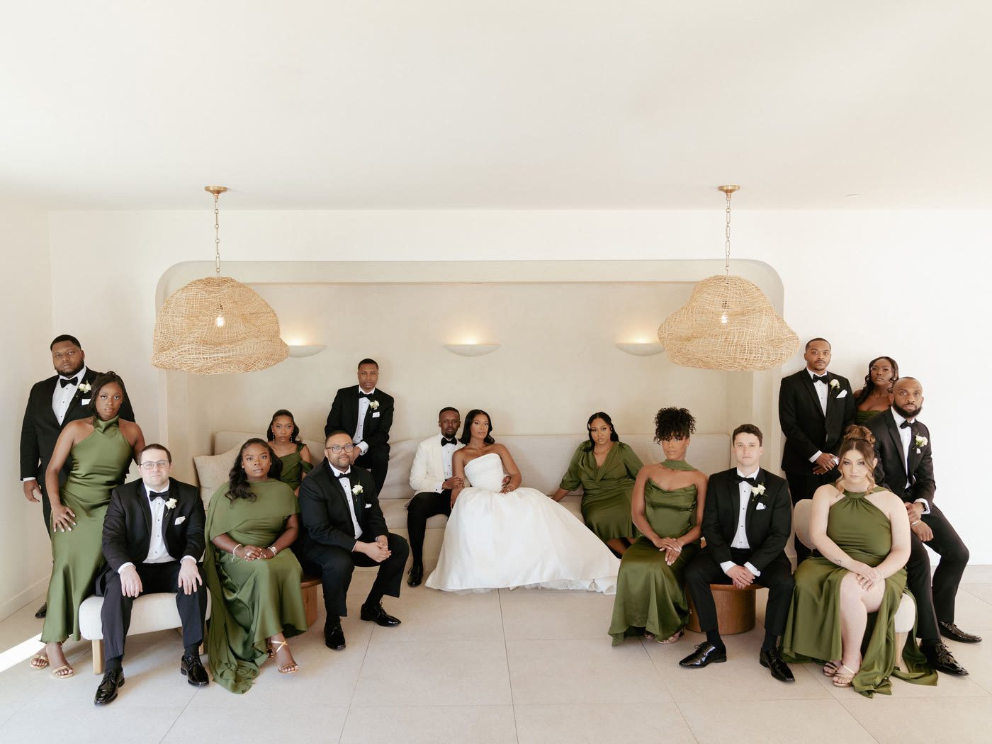 The full wedding party gathered in a cream parlor, olive gowns and black tuxedos