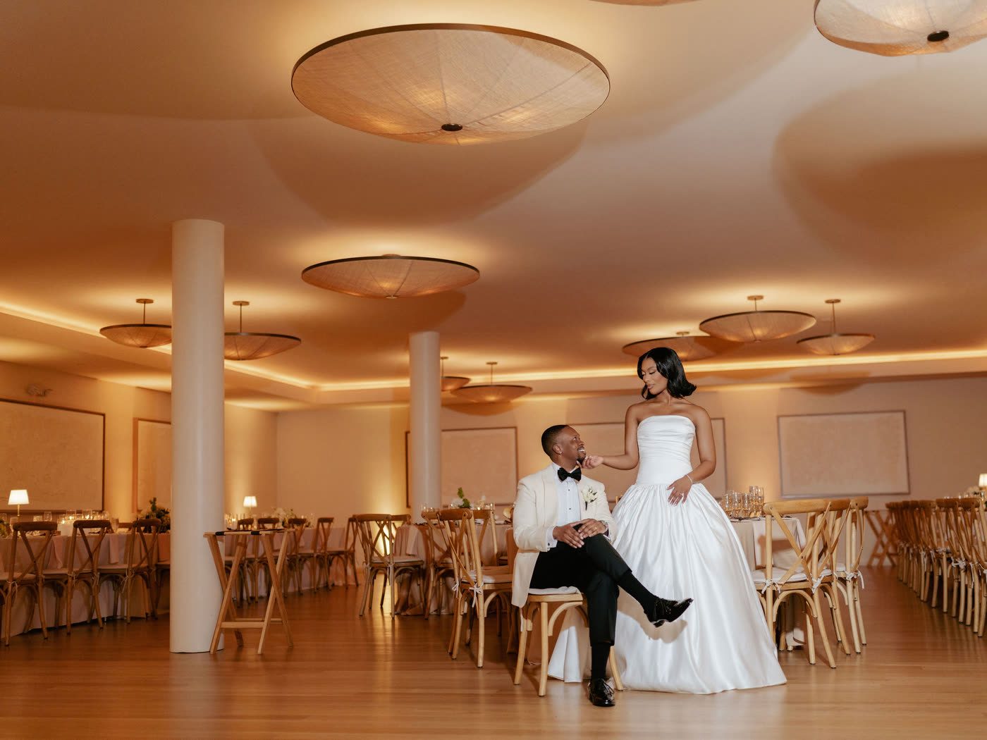 Reception ballroom glowing with warm light, couple among the tables