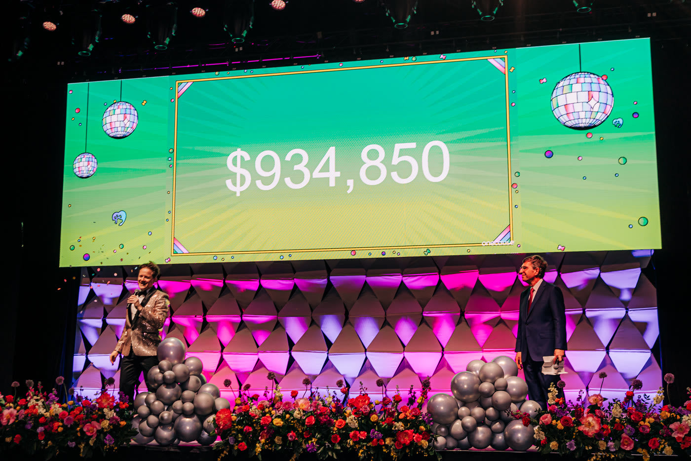 The tally on the screen — florals along the stage edge
