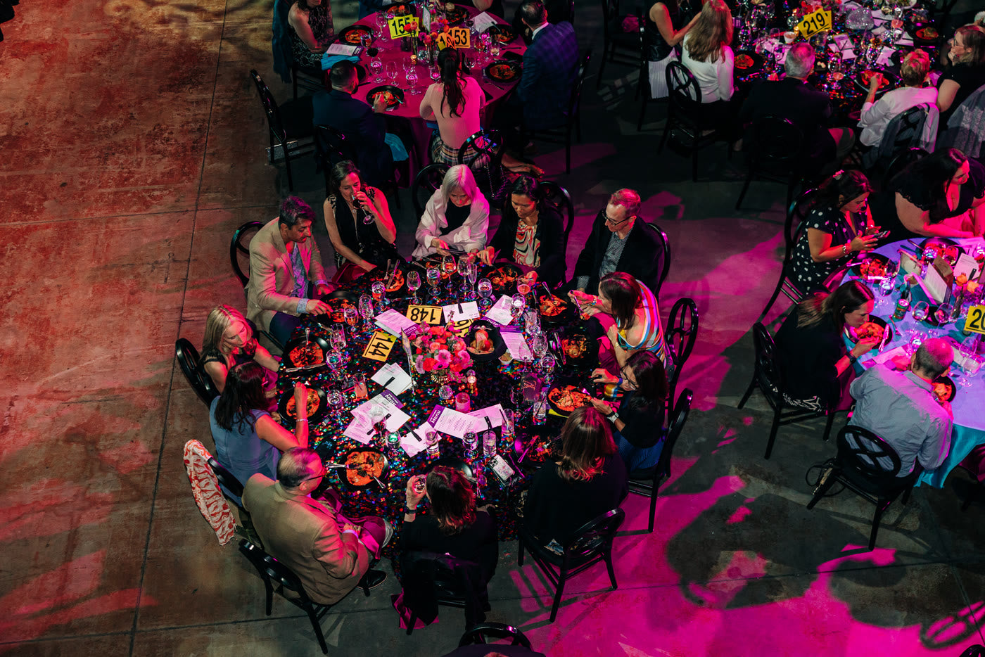Overhead of gala tables mid-celebration, confetti linens and coral florals