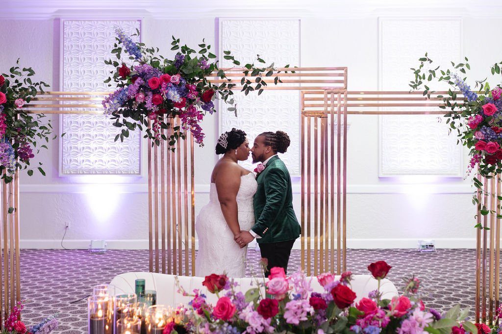 Jewel-toned florals over the arch as the couple kiss