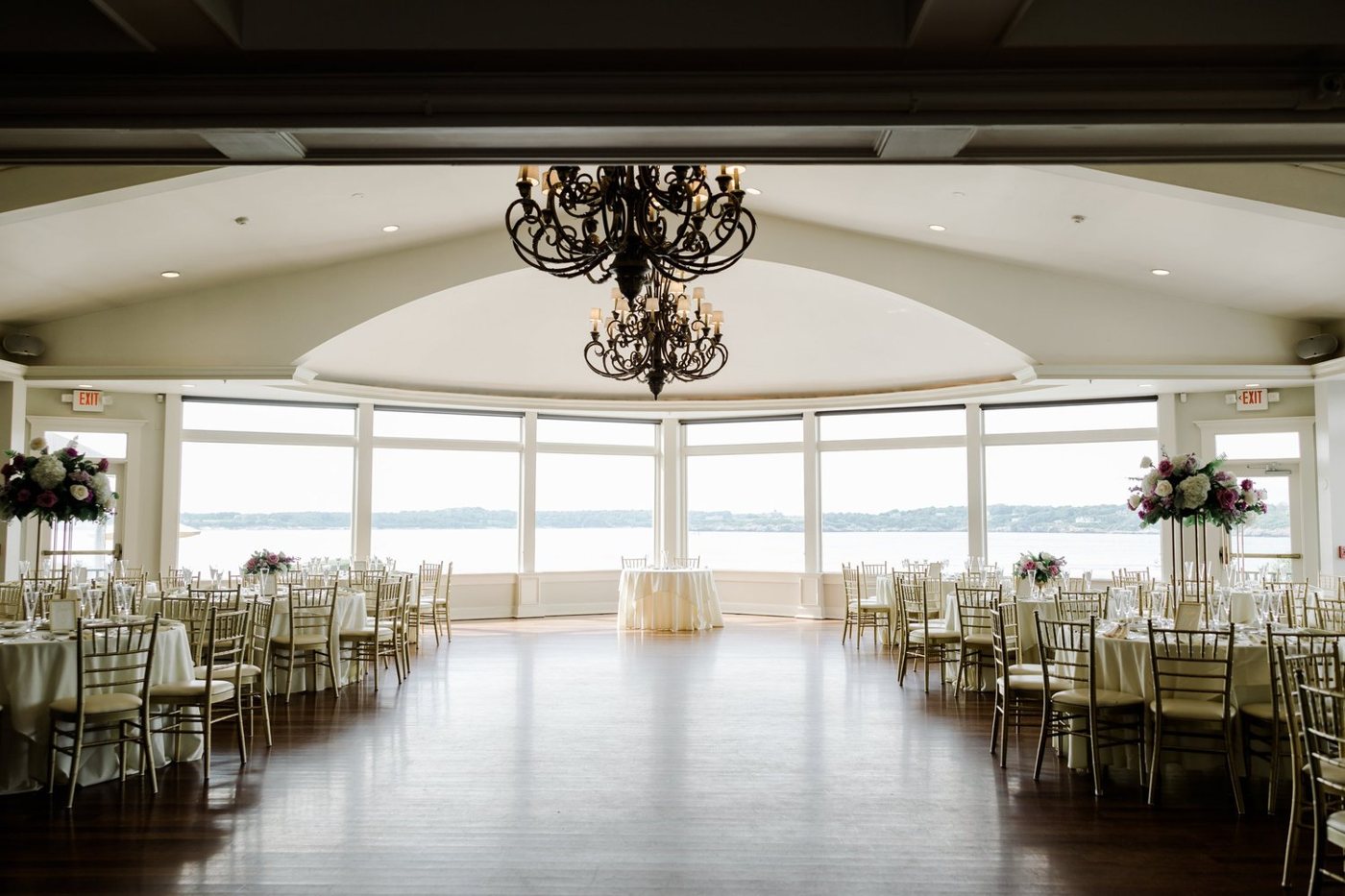 An empty ballroom before the guests arrive, chandeliers lit, the harbor in the windows