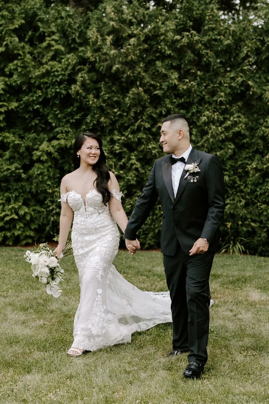 A couple walks hand in hand across a garden lawn