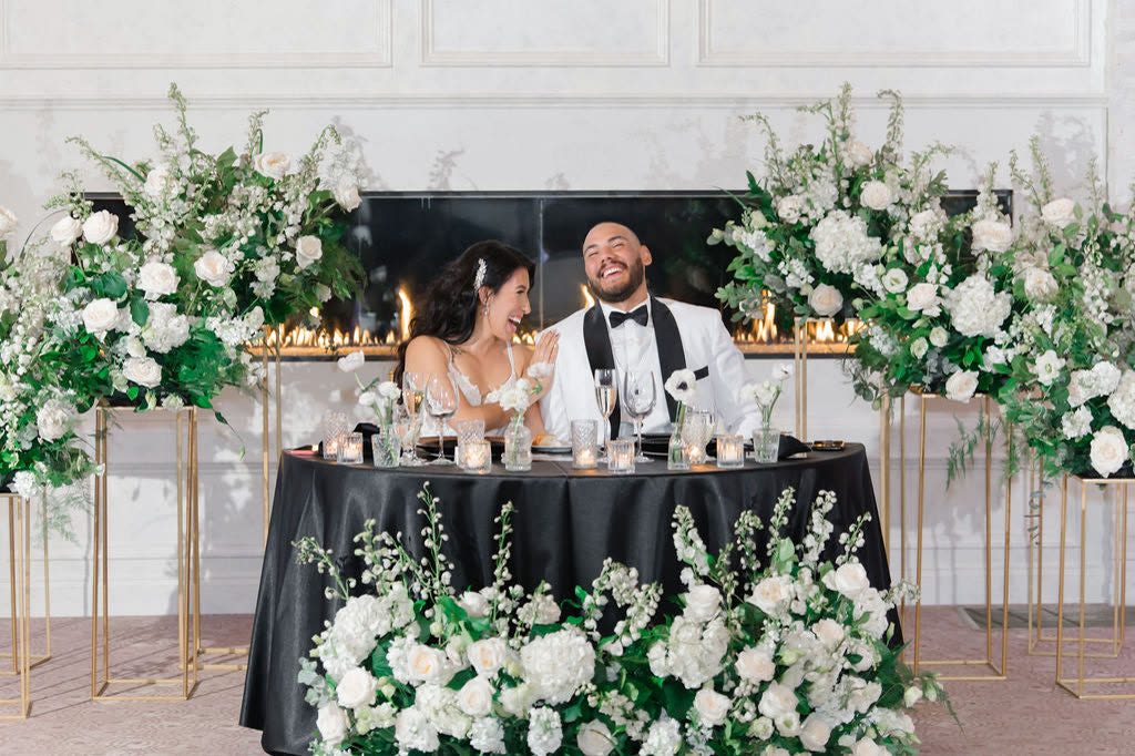 Couple laughing at a sweetheart table framed by white florals